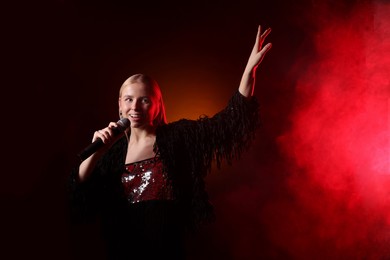 Beautiful singer performing on dark background with red light and smoke