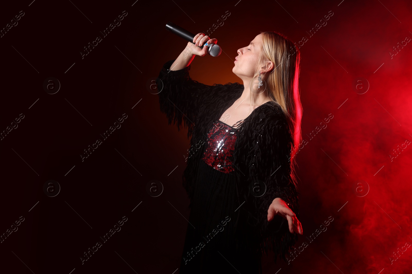 Photo of Beautiful singer performing on dark background with red light and smoke