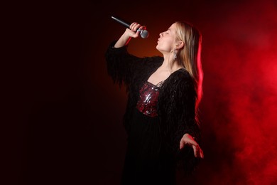 Beautiful singer performing on dark background with red light and smoke