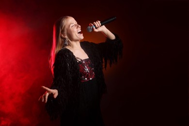 Photo of Beautiful singer performing on dark background with red light and smoke