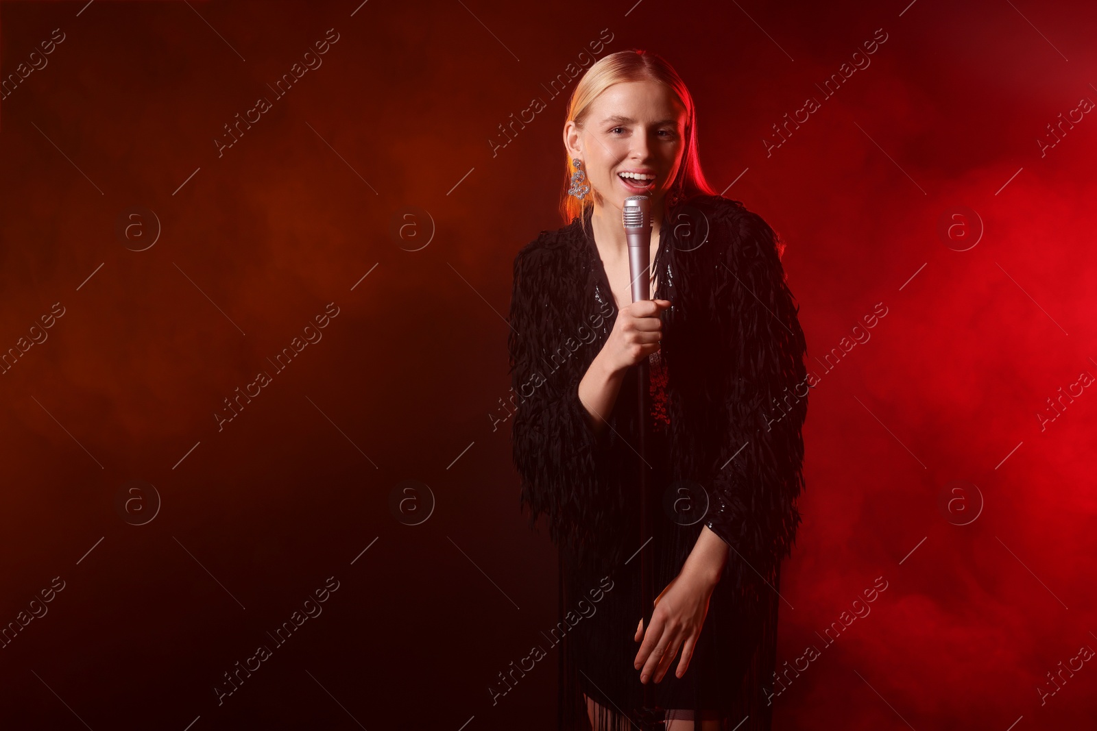 Photo of Beautiful singer performing on dark background with red light and smoke. Space for text