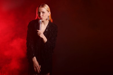 Photo of Beautiful singer performing on dark background with red light and smoke. Space for text