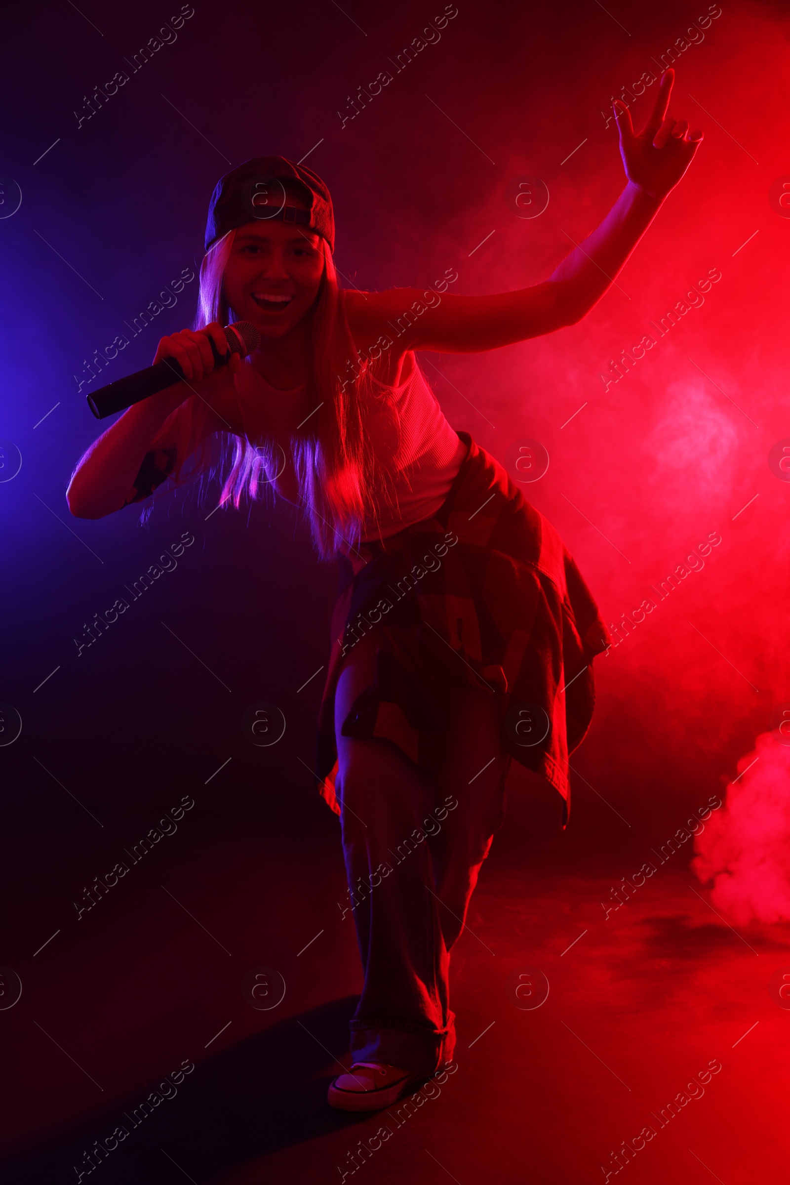 Photo of Talented singer performing on dark background with color lights and smoke