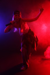 Photo of Talented singer performing on dark background with color lights and smoke