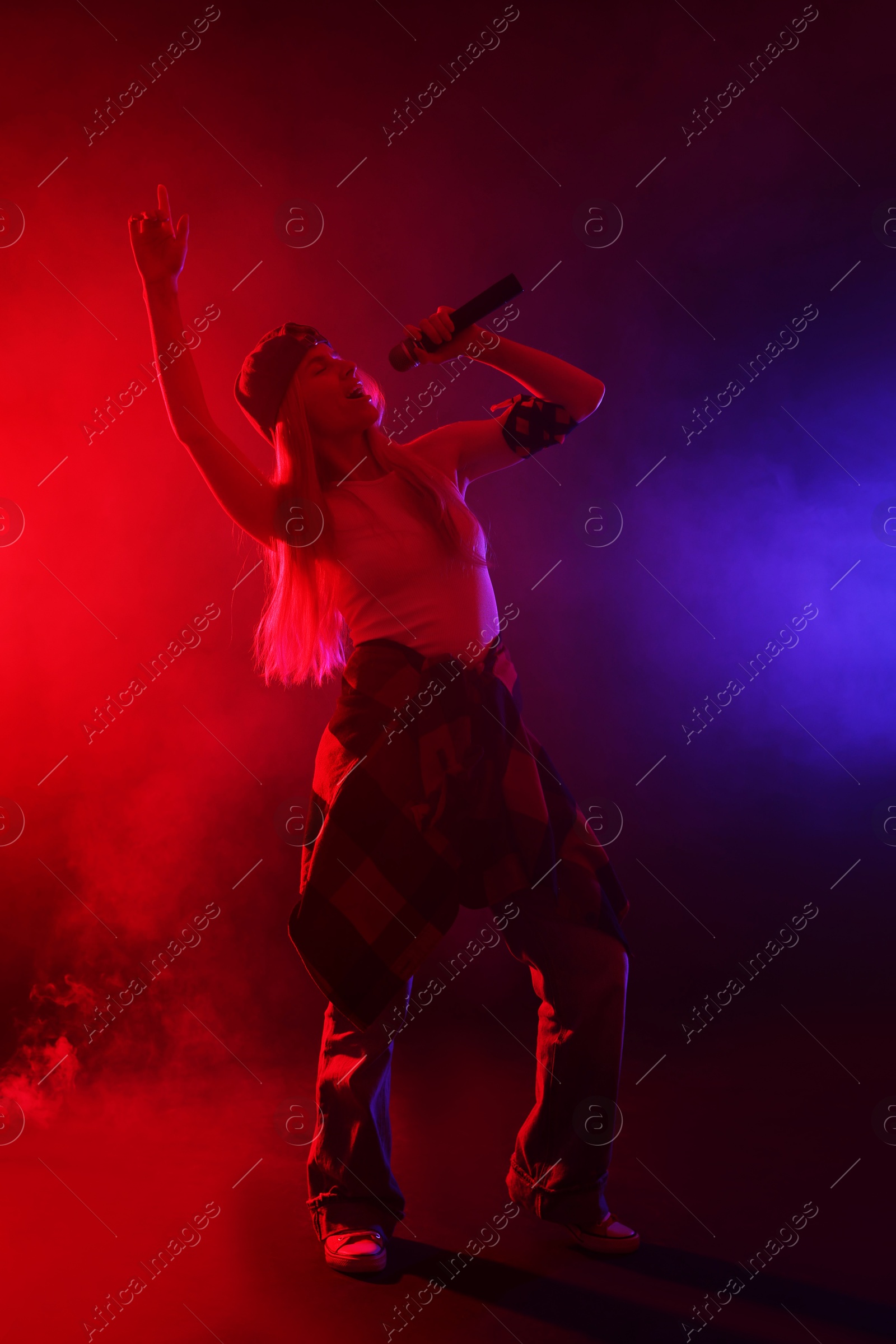 Photo of Talented singer performing on dark background with color lights and smoke