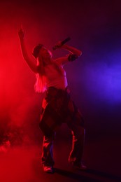 Photo of Talented singer performing on dark background with color lights and smoke