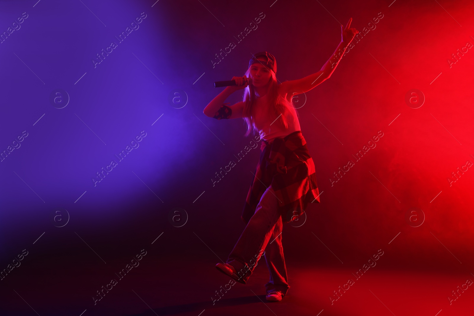 Photo of Talented singer performing on dark background with color lights and smoke