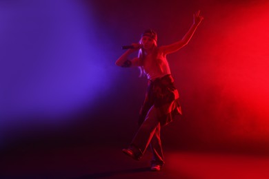 Photo of Talented singer performing on dark background with color lights and smoke