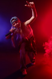 Photo of Talented singer performing on dark background with color lights and smoke