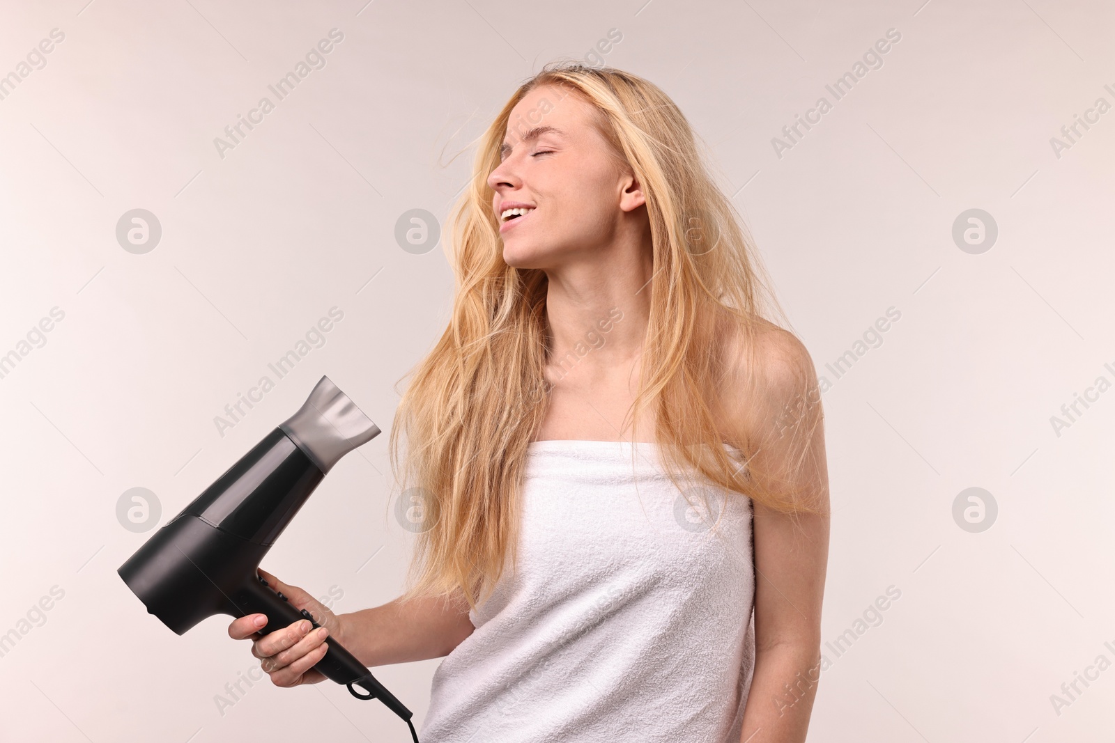 Photo of Beautiful young woman drying her hair with hairdryer on light grey background