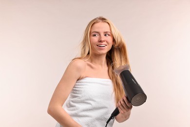 Photo of Beautiful young woman drying her hair with hairdryer on light grey background