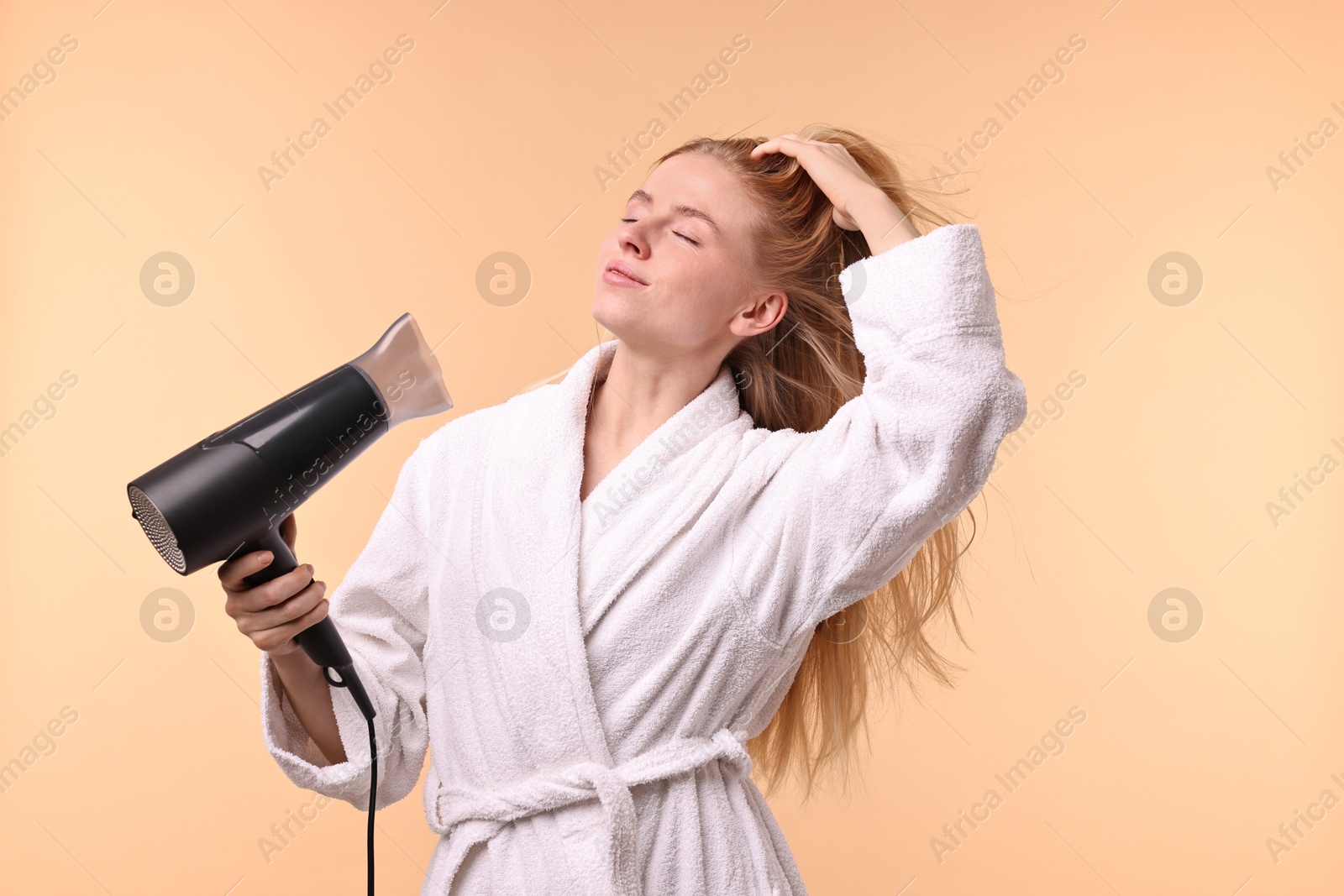 Photo of Beautiful young woman drying her hair with hairdryer on beige background