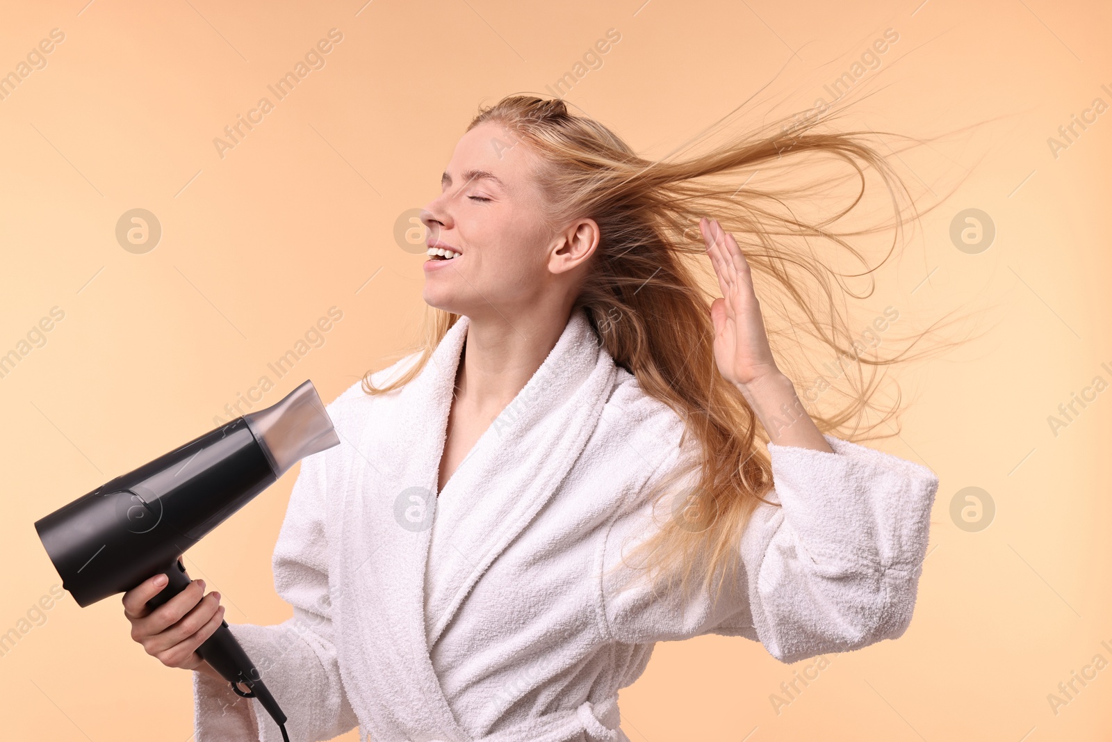 Photo of Beautiful young woman drying her hair with hairdryer on beige background