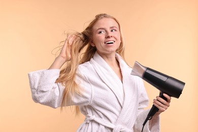 Beautiful young woman drying her hair with hairdryer on beige background