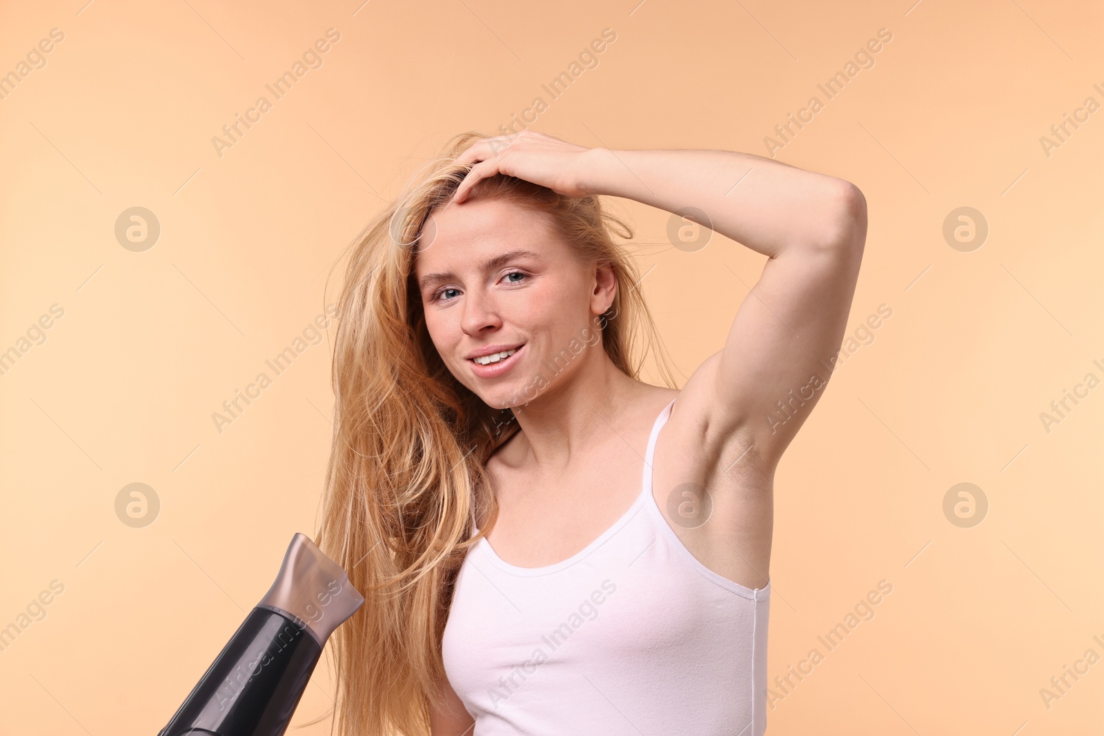 Photo of Beautiful young woman drying her hair with hairdryer on beige background