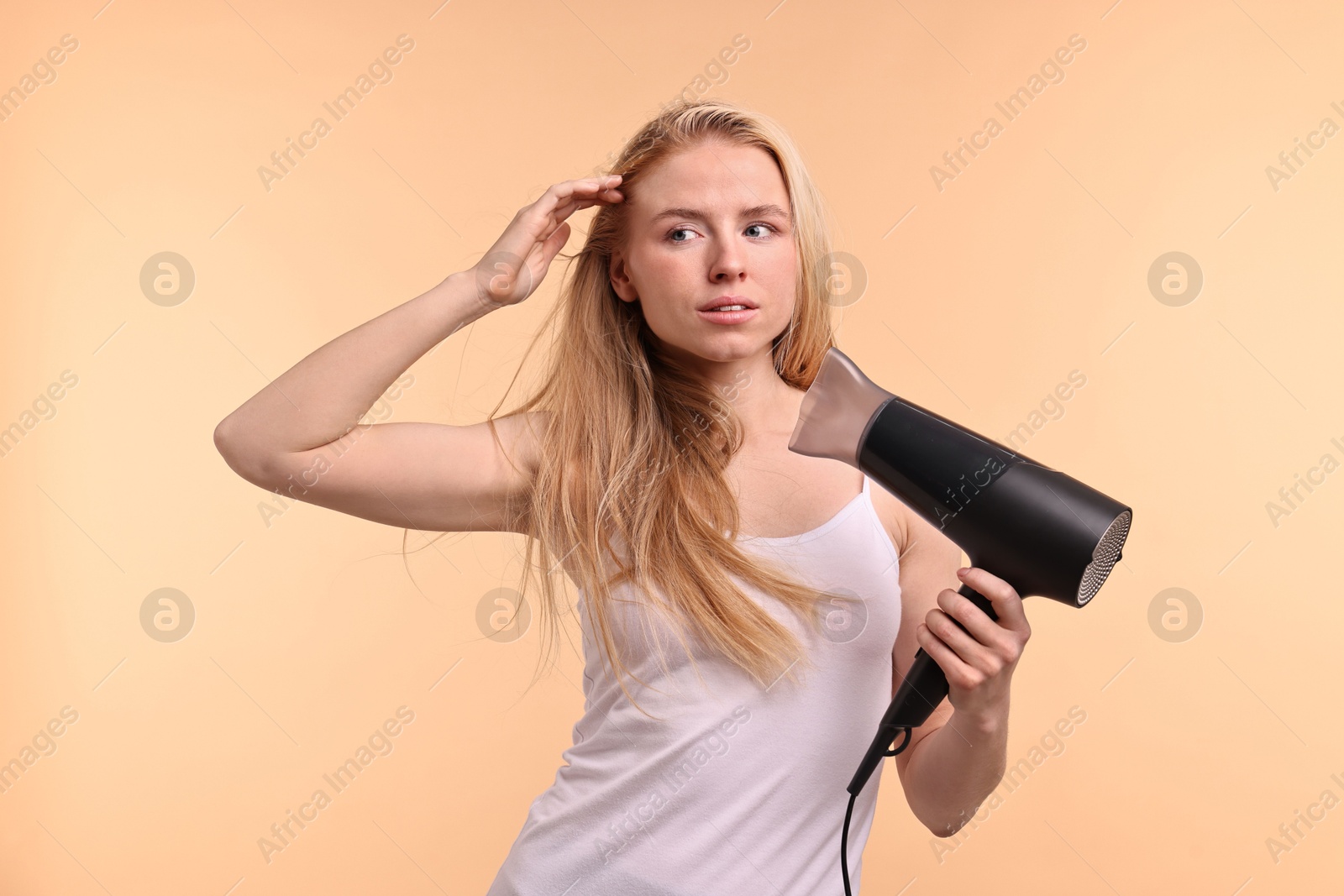 Photo of Beautiful young woman drying her hair with hairdryer on beige background