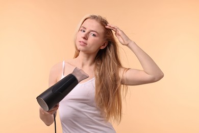 Beautiful young woman drying her hair with hairdryer on beige background