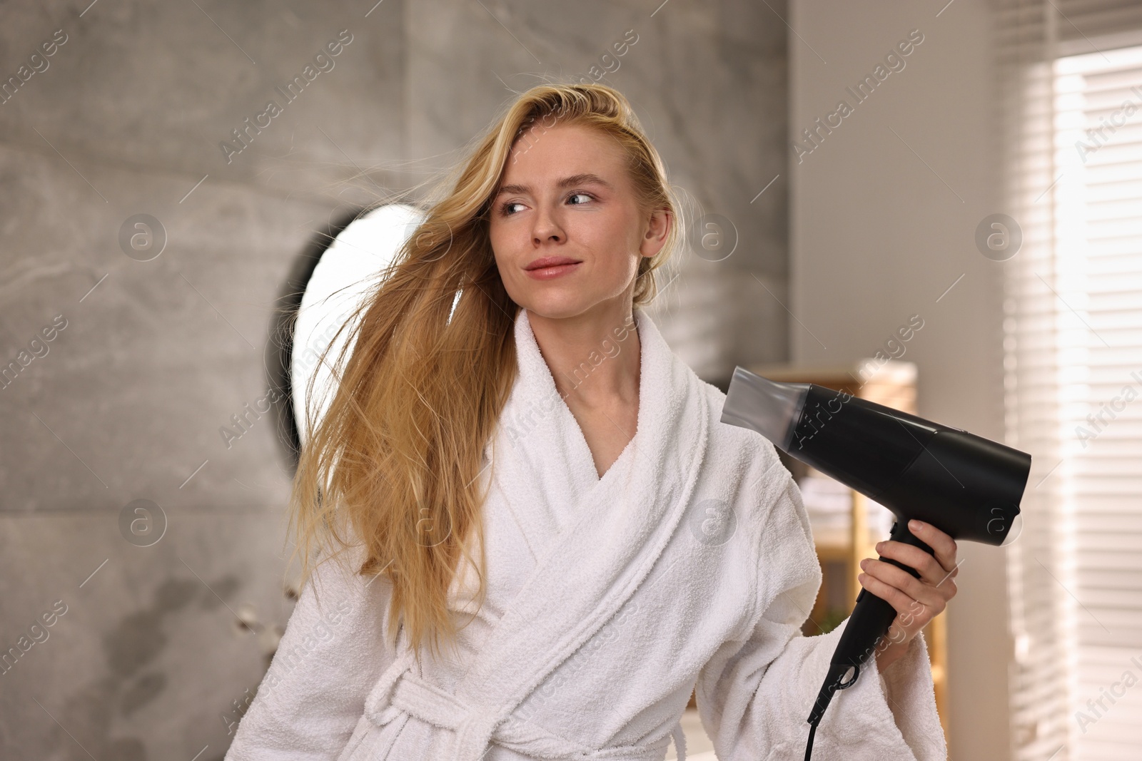 Photo of Beautiful young woman drying her hair in bathroom