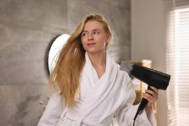 Beautiful young woman drying her hair in bathroom