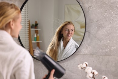 Photo of Beautiful young woman drying her hair near mirror in bathroom