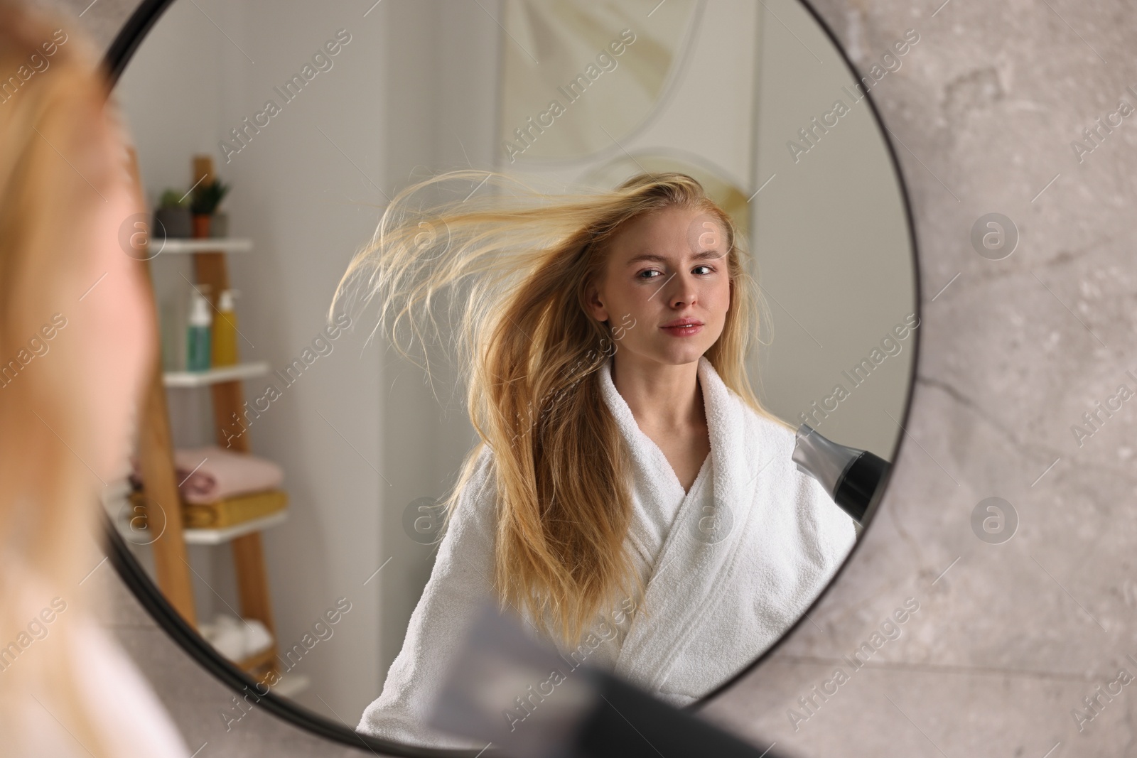 Photo of Beautiful young woman drying her hair near mirror in bathroom