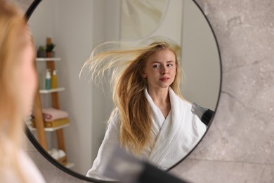 Beautiful young woman drying her hair near mirror in bathroom