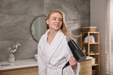 Photo of Beautiful young woman drying her hair in bathroom