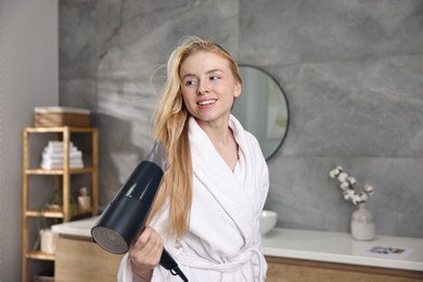 Beautiful young woman drying her hair in bathroom