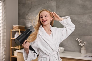 Photo of Beautiful young woman drying her hair in bathroom