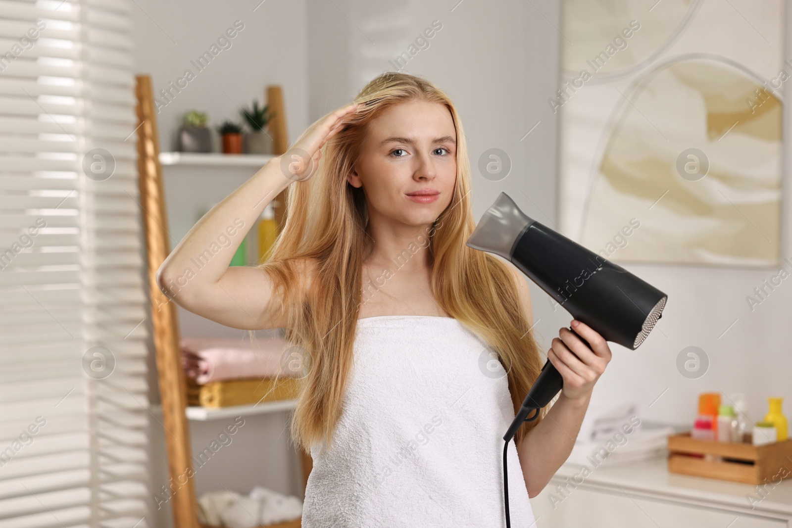 Photo of Beautiful young woman drying her hair in bathroom