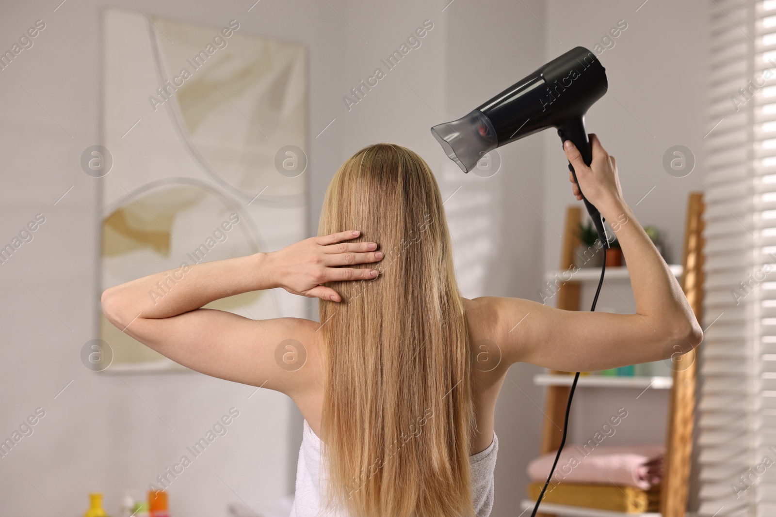 Photo of Beautiful young woman drying her hair in bathroom, back view