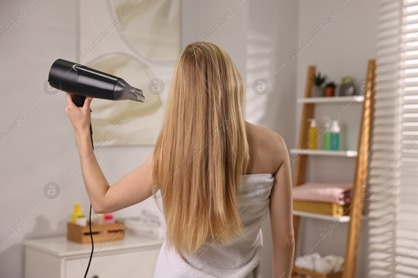 Photo of Beautiful young woman drying her hair in bathroom, back view