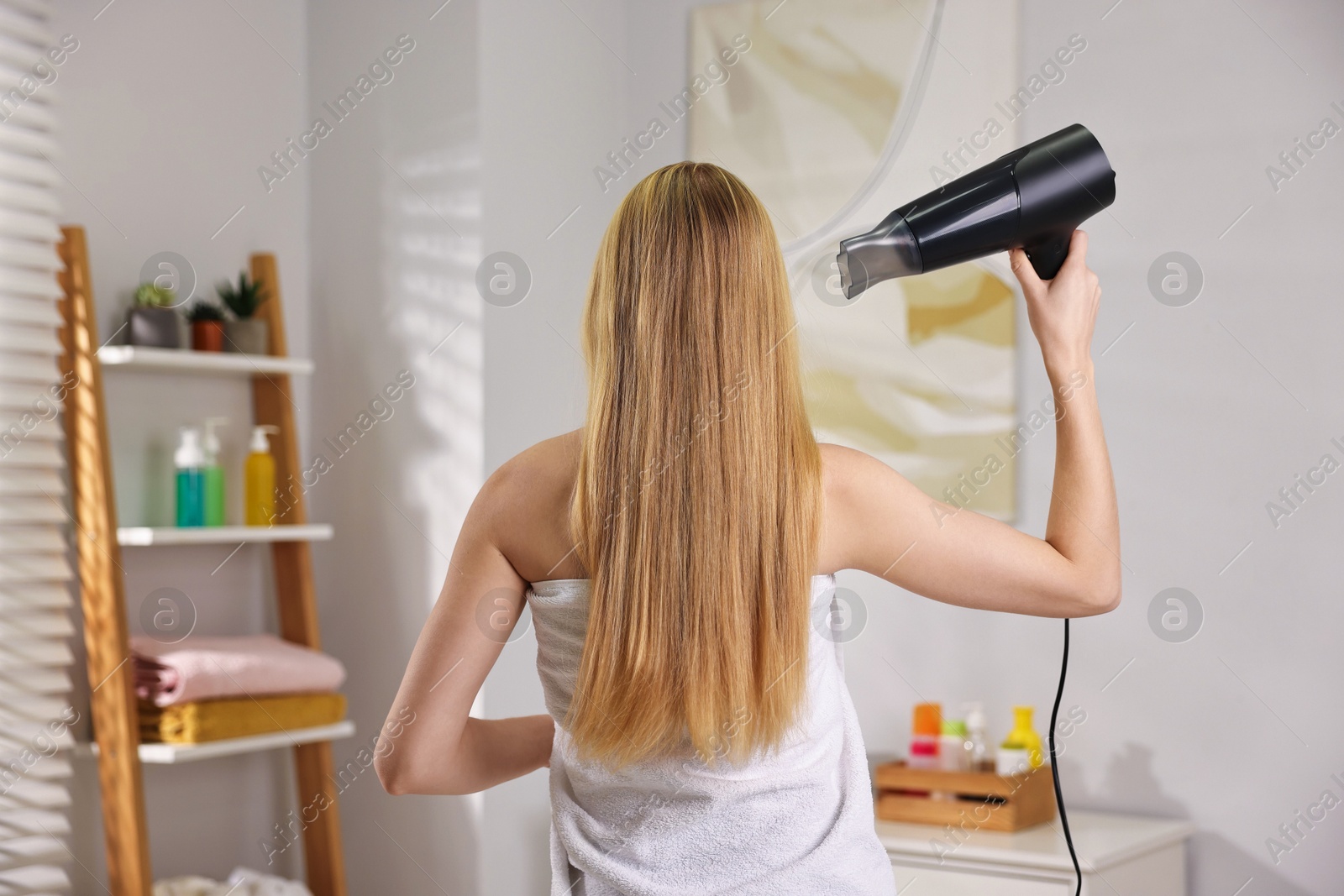 Photo of Beautiful young woman drying her hair in bathroom, back view