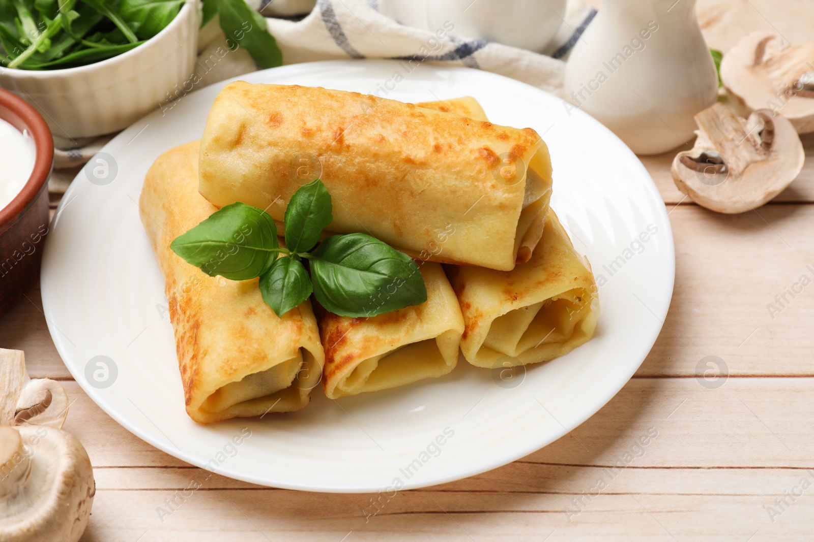 Photo of Delicious rolled crepes with basil and mushrooms on wooden table, closeup