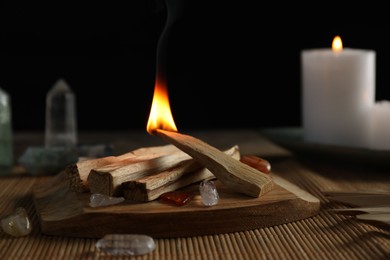 Photo of Burning palo santo stick, gemstones and candles on table, closeup