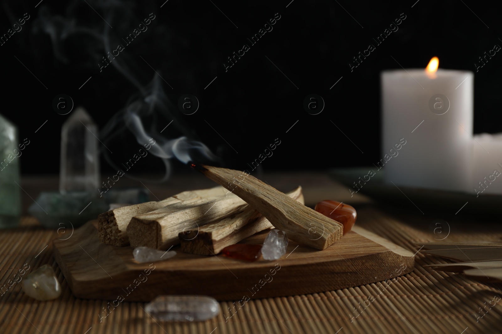 Photo of Smoldering palo santo stick, gemstones and burning candle on table, closeup