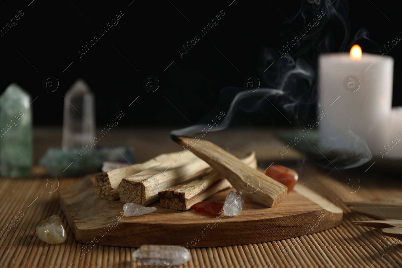 Photo of Smoldering palo santo stick, gemstones and burning candle on table, closeup