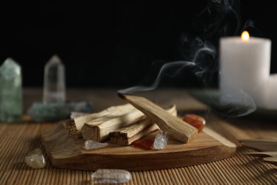 Photo of Smoldering palo santo stick, gemstones and burning candle on table, closeup