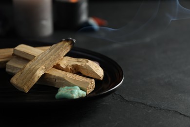 Photo of Smoldering palo santo stick and gemstone on black table, closeup. Space for text