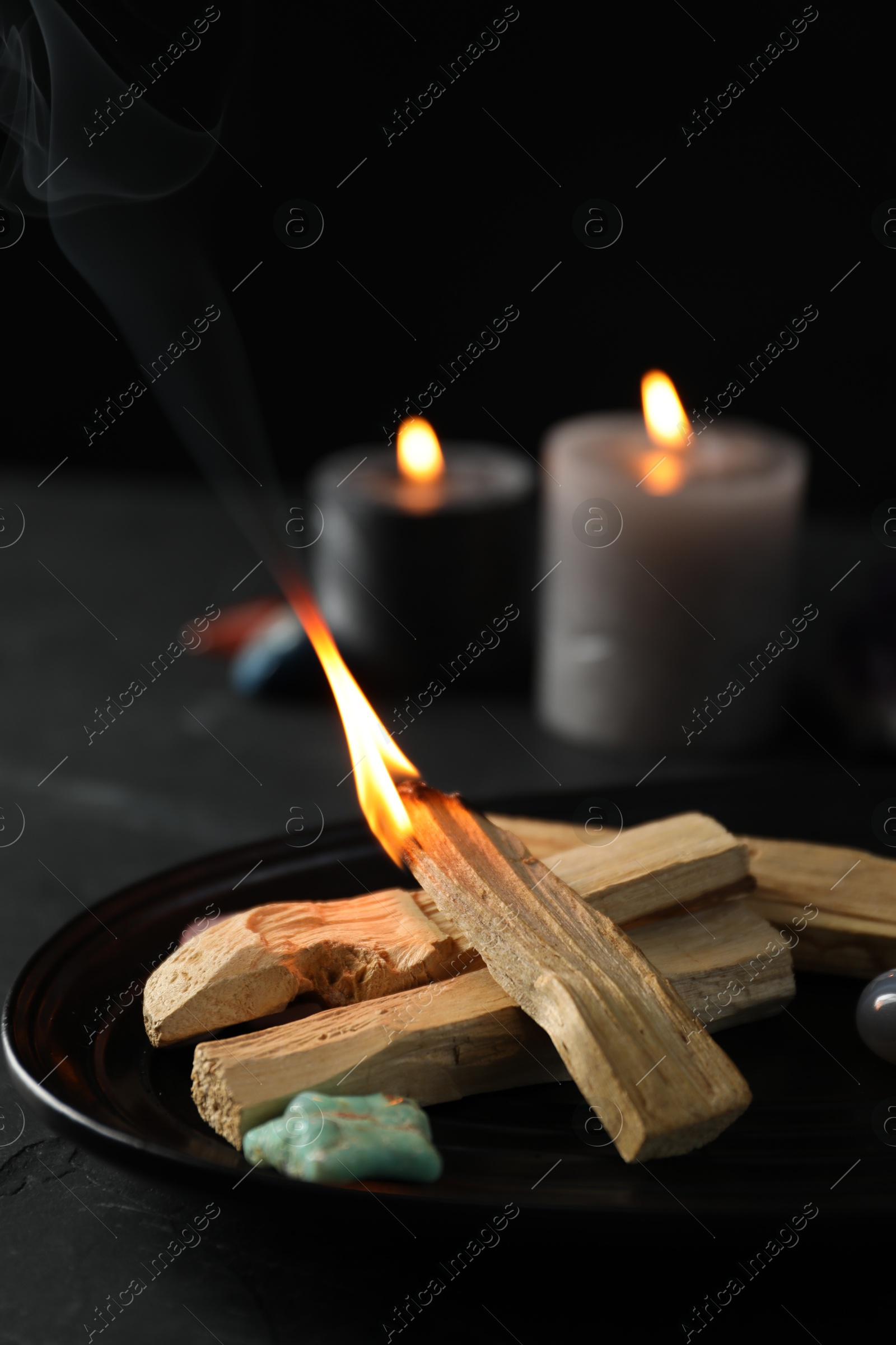 Photo of Burning palo santo stick, gemstone and candles on black table, closeup