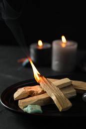 Photo of Burning palo santo stick, gemstone and candles on black table, closeup