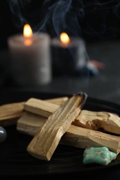 Photo of Smoldering palo santo stick, gemstone and burning candles on table, closeup