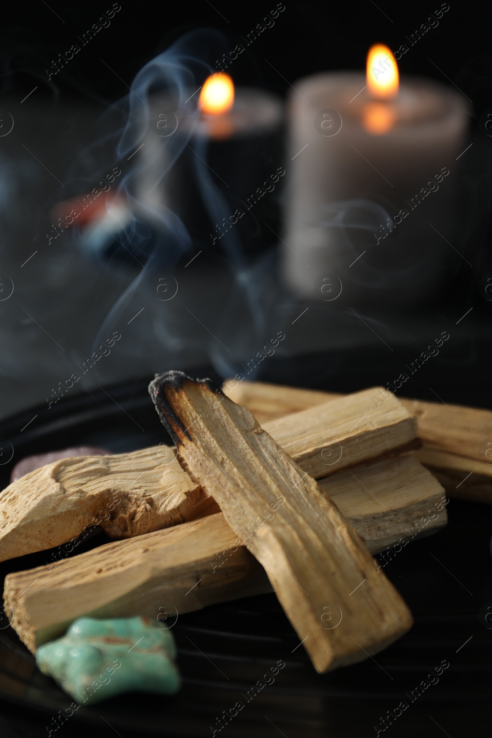 Photo of Smoldering palo santo stick, gemstone and burning candles on table, closeup