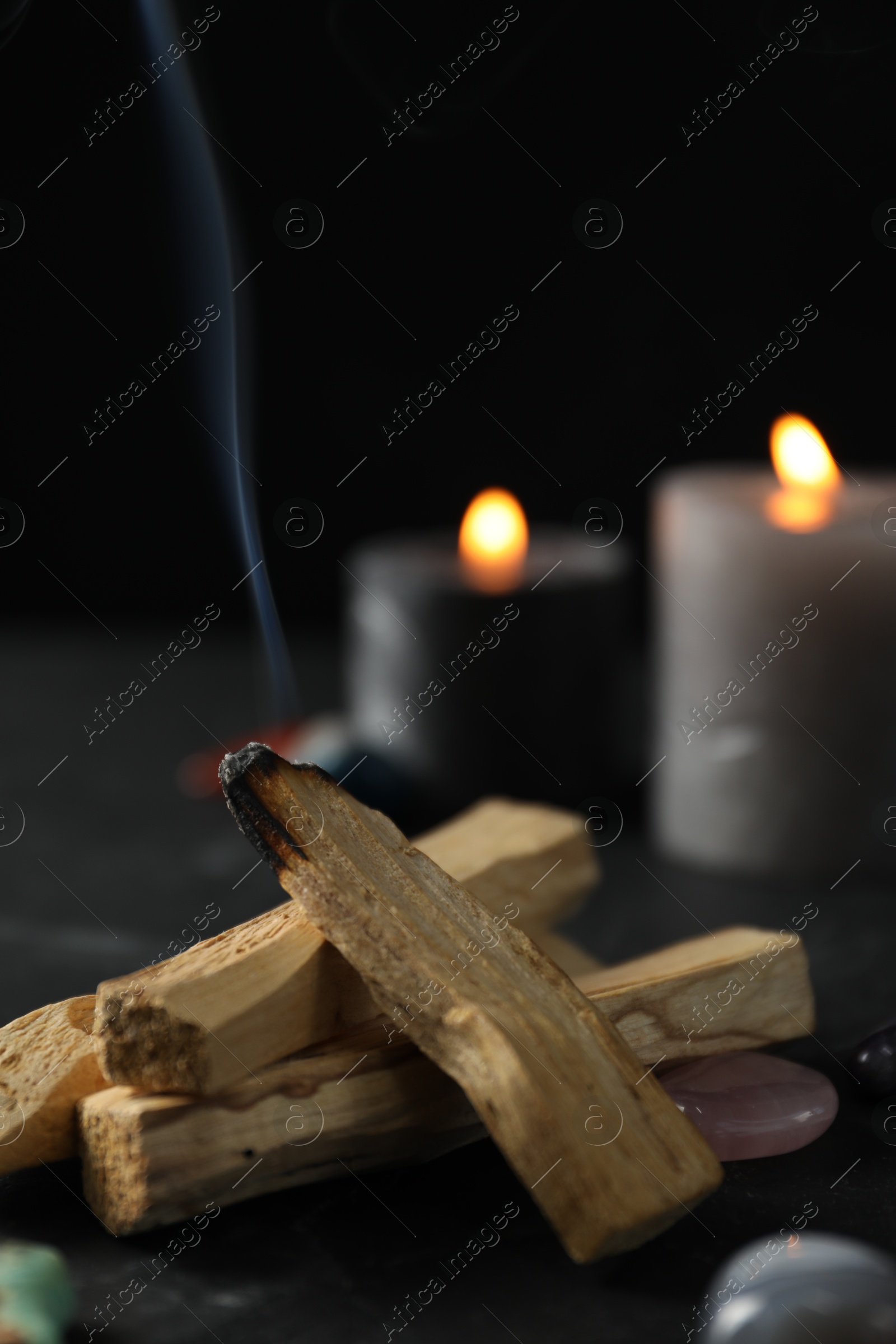 Photo of Smoldering palo santo stick, gemstones and burning candles on black table, closeup