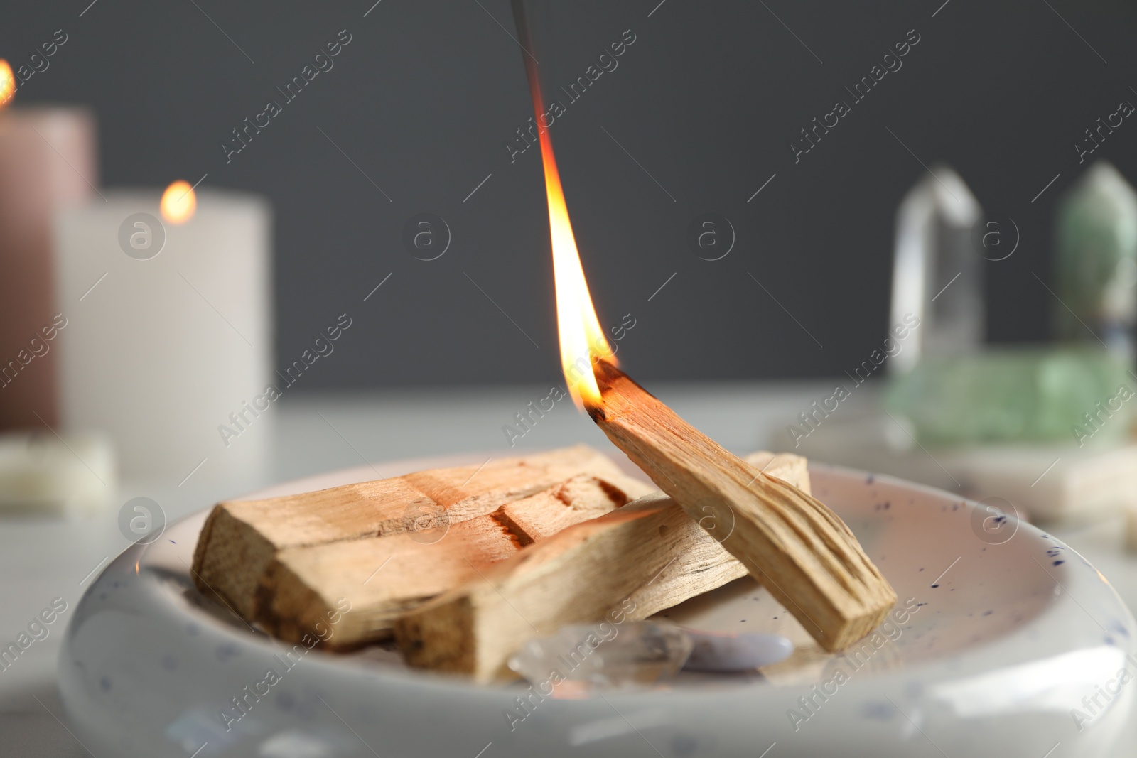 Photo of Burning palo santo stick and gemstones on table, closeup