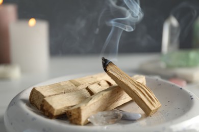 Photo of Smoldering palo santo stick and gemstones on table, closeup