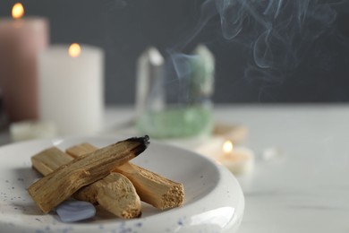 Photo of Smoldering palo santo stick and gemstone on table, closeup. Space for text