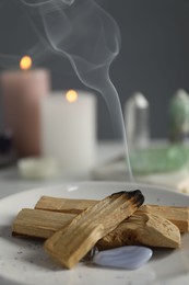 Photo of Smoldering palo santo stick and gemstones on table, closeup