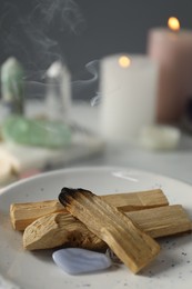 Photo of Smoldering palo santo stick and gemstones on table, closeup