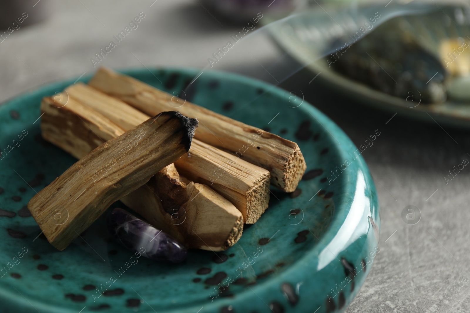 Photo of Smoldering palo santo stick and gemstone on light grey table, closeup